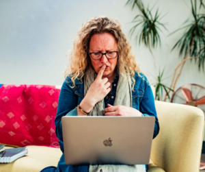 Woman on sofa, with her finger to her mouth, looking at her computer in a confused way.